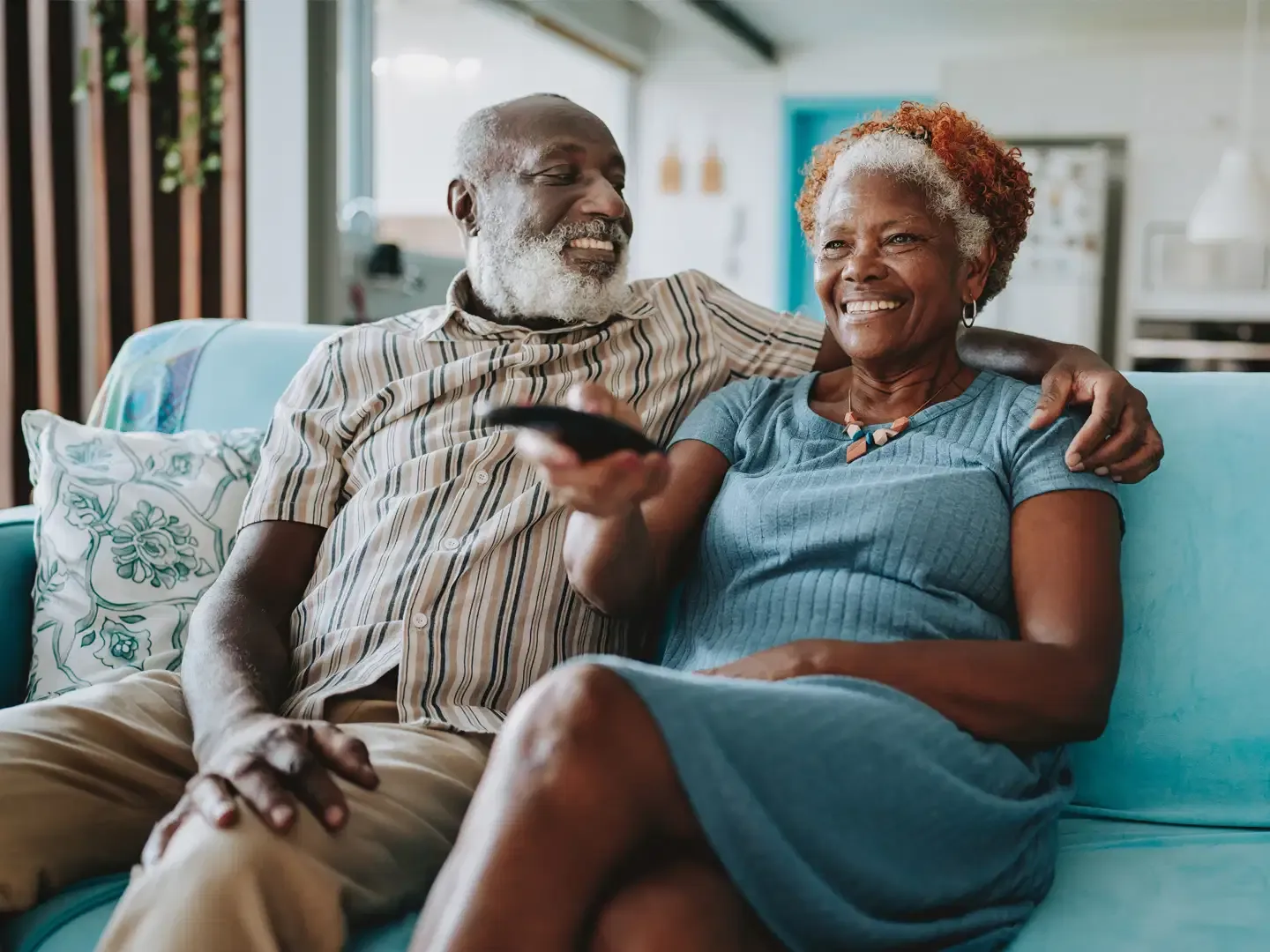 A smiling senior couple sitting on a blue sofa while watching TV together.